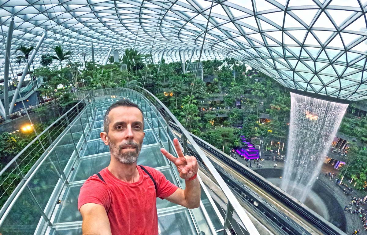Travel blogger Ivan Kralj standing on Mastercard Canopy Bridge with Rain Vortex in the background, the world's largest indoor waterfall in a stunning Jewel complex of Singapore Changi Airport; photo by Ivan Kralj.