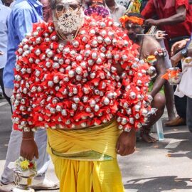 An older Hindu devotee carrying koodam mulle kavadi - milk pots pierced on his torso, and with cheeks and tongue pierced with little spears (alavu kavadi) in honor of Lord Murugan, during Thaipusam Festival in Penang, Malaysia; photo by Ivan Kralj.
