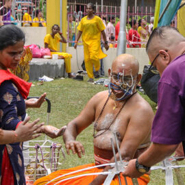 A man with pierced facial skin sitting near Waterfall Hilltop Temple during Thaipusam in Penang, Malaysia; photo by Ivan Kralj.