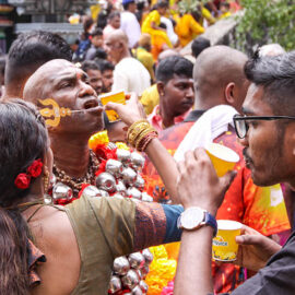 A woman assisting with drinking to Hindu devotee with alavu kavadi (pierced cheeks and tongue), during Thaipusam in Penang, Malaysia; photo by Ivan Kralj.