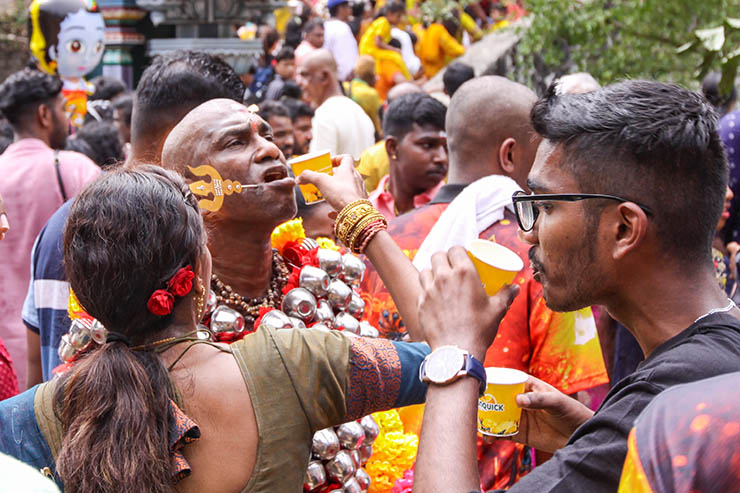 A woman assisting with drinking to Hindu devotee with alavu kavadi (pierced cheeks and tongue), during Thaipusam in Penang, Malaysia; photo by Ivan Kralj.