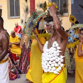 Two men with pierced torsos with hanging objects (koodam mulle) and milk pots on top of their heads (paal kudam), while women behind them carry thol kavadi on shoulders, during Thaipusam in Penang, Malaysia; photo by Ivan Kralj.