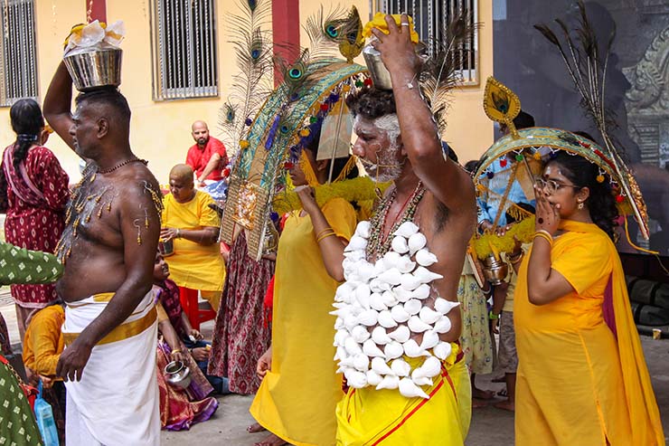 Two men with pierced torsos with hanging objects (koodam mulle) and milk pots on top of their heads (paal kudam), while women behind them carry thol kavadi on shoulders, during Thaipusam in Penang, Malaysia; photo by Ivan Kralj.