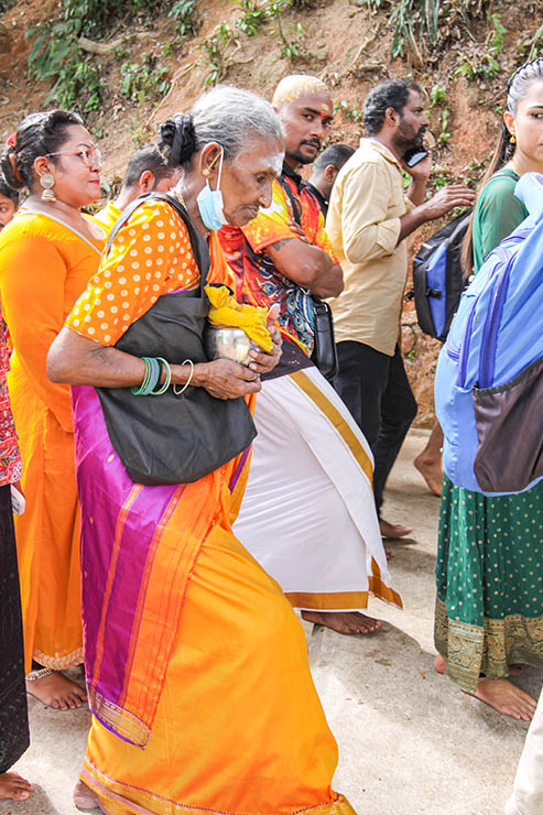 An older Hindu woman carrying a milk pot (paal kudam) in her arms as she climbs the stairs to Waterfall Temple during Thaipusam Festival in Penang, Malaysia; photo by Ivan Kralj.