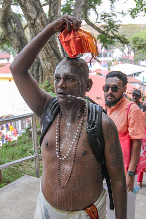 A Hindu man with pierced cheeks carrying a milk pot (paal kudam) on his head, while milk pours down his bare torso, during Thaipusam Festival in Penang, Malaysia; photo by Ivan Kralj.