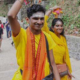 Young man and woman smiling while carrying milk pots (paal kudam) on their heads to the Waterfall Temple atop the hill il Penang, Malaysia, during Thaipusam; photo by Ivan Kralj.
