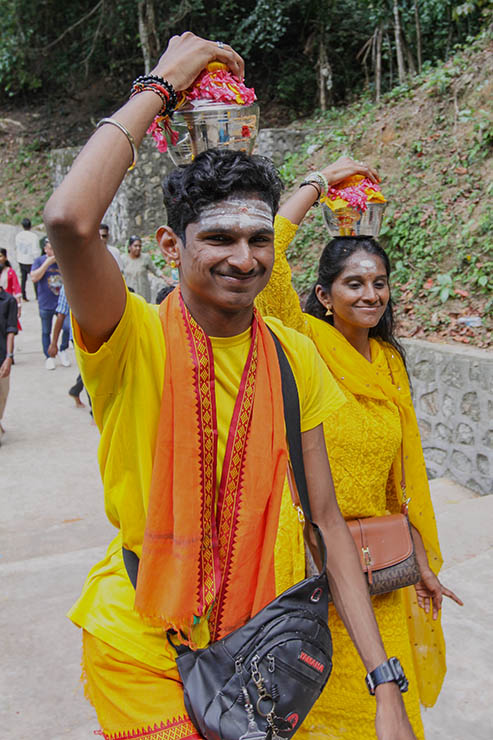 Young man and woman smiling while carrying milk pots (paal kudam) on their heads to the Waterfall Temple atop the hill il Penang, Malaysia, during Thaipusam; photo by Ivan Kralj.