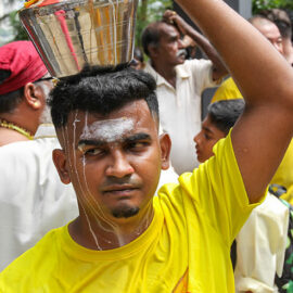 A Hindu man holding a milk pot (paal kudam) on his head, while milk pours down his face, during Thaipusam Festival in Penang, Malaysia; photo by Ivan Kralj.