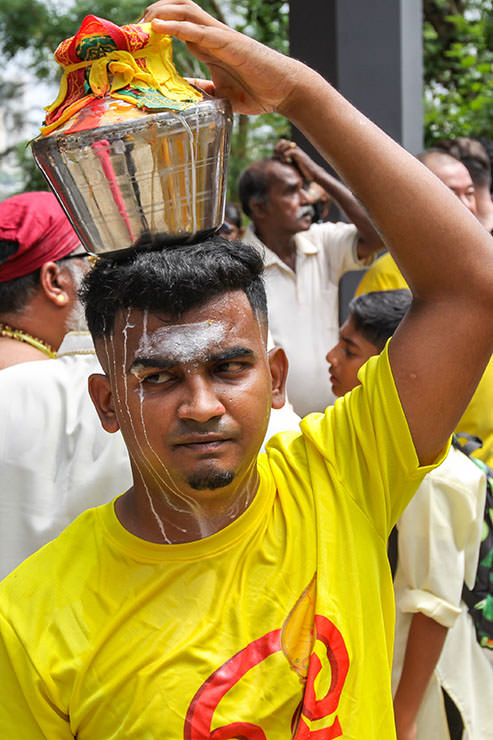 A Hindu man holding a milk pot (paal kudam) on his head, while milk pours down his face, during Thaipusam Festival in Penang, Malaysia; photo by Ivan Kralj.