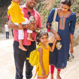 A smiling Hindu family, parents with a girl and a boy, carrying milk pots (paal kudam) for Thaipusam in Penang, Malaysia; photo by Ivan Kralj.