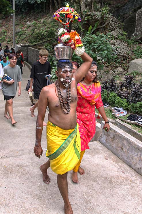 A shirtless Hindu man with pierced cheeks and tongue (alavu kavadi) carrying a milk pot (paal kudam) on his head, during Thaipusam Festival in Penang, Malaysia; photo by Ivan Kralj.