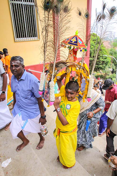 A young boy carrying a thol kavadi on his shoulders up the stairs during Thaipusam in Penang, Malaysia; photo by Ivan Kralj.