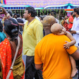 Despite the noise, a bald-shaved baby sleeping while resting his head on the shoulder of his bald-shaved father watching the crowds at Thaipusam in Penang, Malaysia; photo by Ivan Kralj.