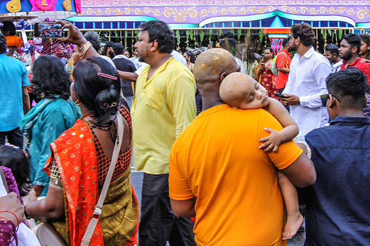 Despite the noise, a bald-shaved baby sleeping while resting his head on the shoulder of his bald-shaved father watching the crowds at Thaipusam in Penang, Malaysia; photo by Ivan Kralj.