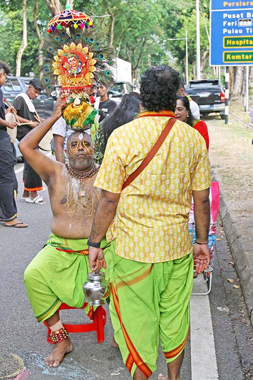 A seated Hindu devotee holding paal kudam milk pot on his head, with alavu kavadi - pierced cheeks and forehead, during Thaipusam in Penang, Malaysia; photo by Ivan Kralj.