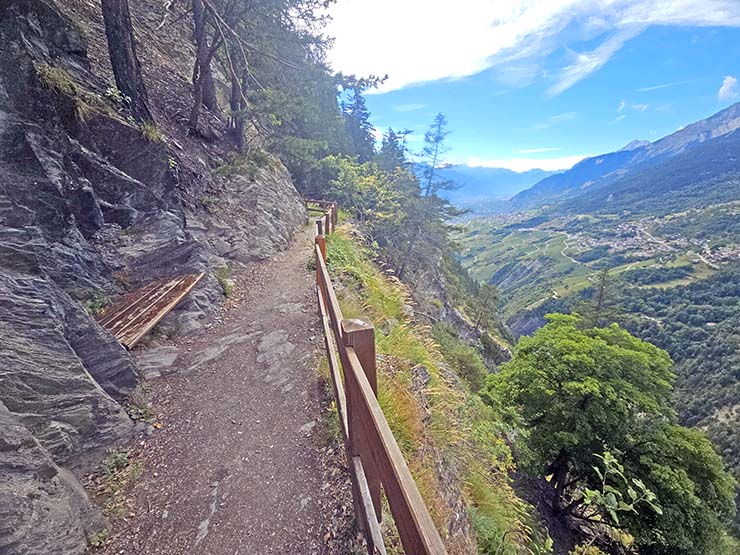 A bench at the viewpoint of Bisse du Torrrent Neuf, opening panoramic views of the Morge and Rhone Valleys, and Alps peaks in the background; photo by Ivan Kralj.