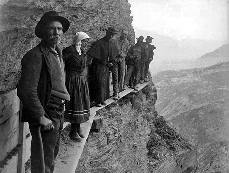 Vintage photograph of Swiss farmers, workers, and a priest, standing on the wooden planks on the cliffs of the Prabé Mountain where they built Bisse du Torrent Neuf; photograph from the 1930s, copyright Bisse de Saviese.