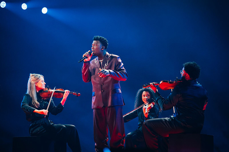 Claude, a Congolese musician performing "C’est La Vie" for Netherlands at Eurovision in Basel, Switzerland, surrounded by violinists; photo by Sarah Louise Bennett / EBU.