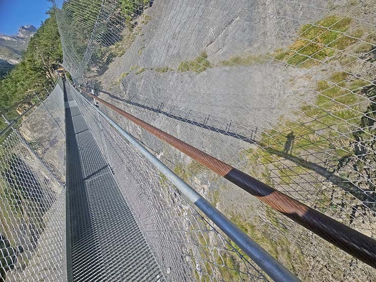 Second suspension bridge at Bisse de Saviese hike, with side netting protecting from the rockfall, there's a shadow of a photographer visible on the floor of the gorge; photo by Ivan Kralj.