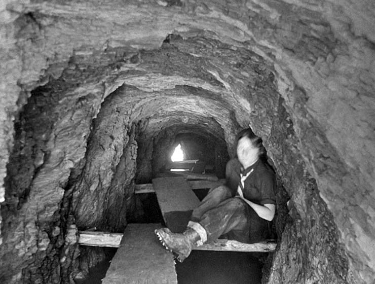 A vintage photograph of a person inside the Tunnel du Mougerin, dug through the mountain on the Bisse du Torrent Neuf trail; one had to crawl over wooden planks to get through; copyright Bisse de Saviese.