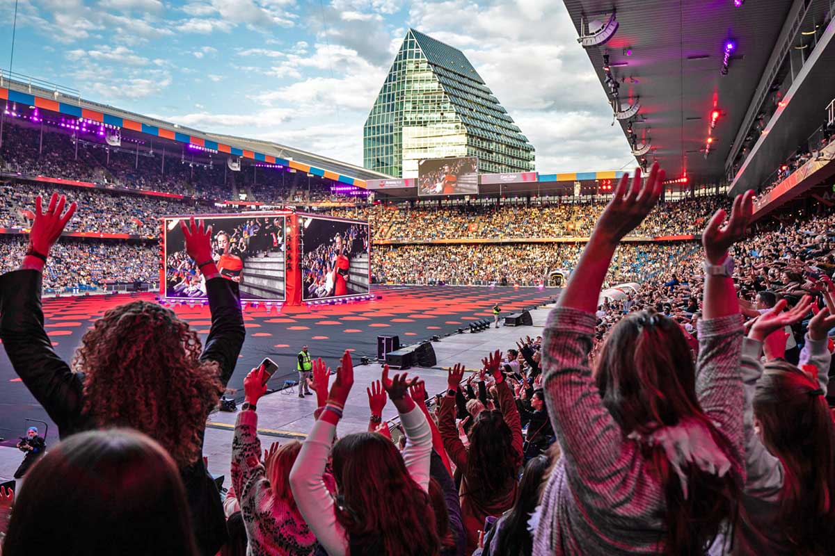 Enthusiastic crowd at St. Jakob-Park stadium raising hadns during Arena Plus Eurovision pre-show; photo by Mood Studios AG.