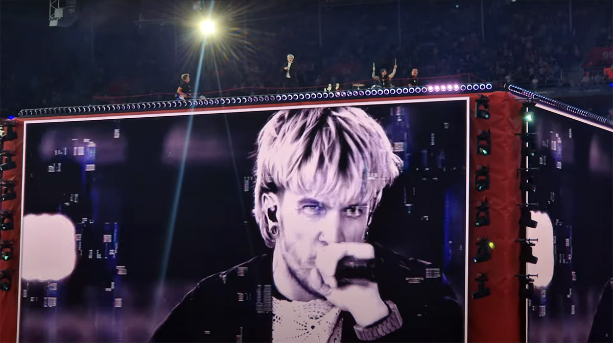Baby Lasagna performing "Rim Tim Tagi Dim" atop a cube-shaped stage at St. Jakob-Park stadium in Basel, Switzerland, during Arena Plus Eurovision pre-show, his act being interfered with controversial visual glitches on screen; screenshot from Luca's Space YouTube footage by Pipeaway.