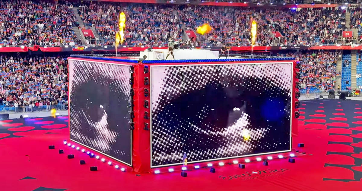 Baby Lasagna band performing "Rim Tim Tagi Dim" in Arena Plus, during a Eurovision pre-show at St. Jakob-Park stadium, atop a cube stage that briefly displays a halftone black-and-white eye flicker; screenshot from Point Switzerland YouTube footage by Pipeaway.