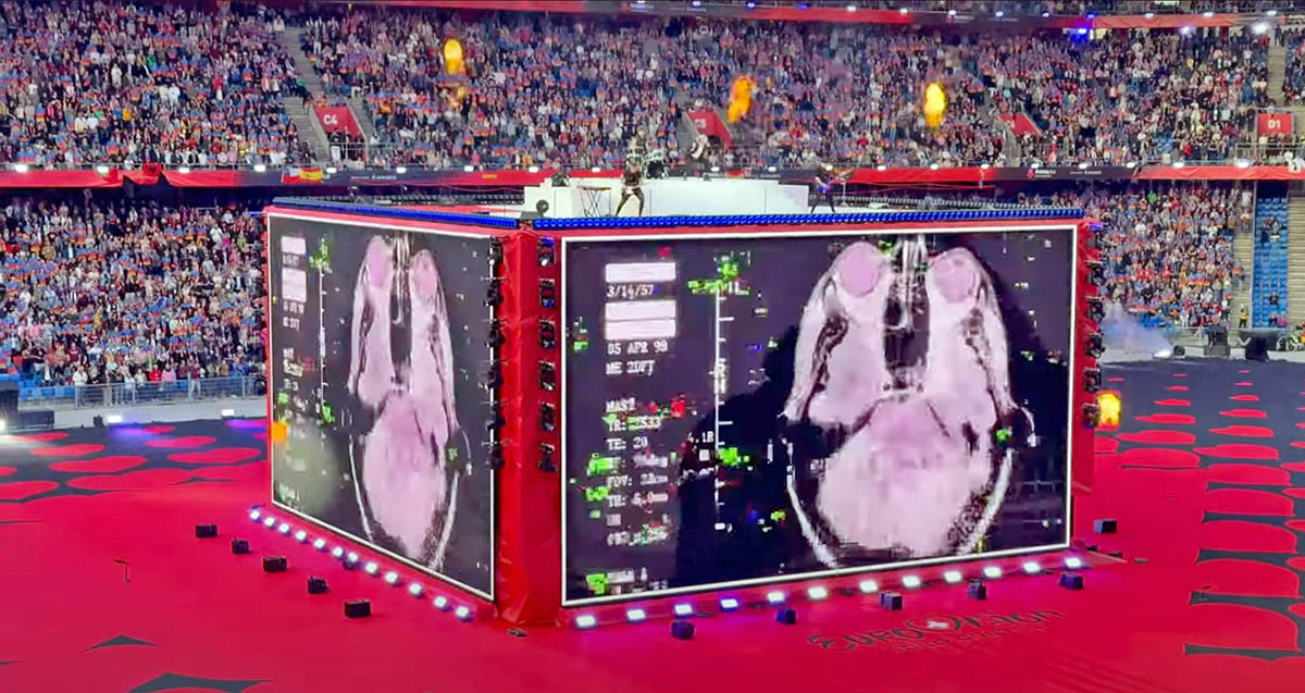 Baby Lasagna band performing "Rim Tim Tagi Dim" in Arena Plus, during a Eurovision pre-show at St. Jakob-Park stadium, atop a cube stage that briefly displays an MRI scan of someone's head; screenshot from Point Switzerland YouTube footage by Pipeaway.