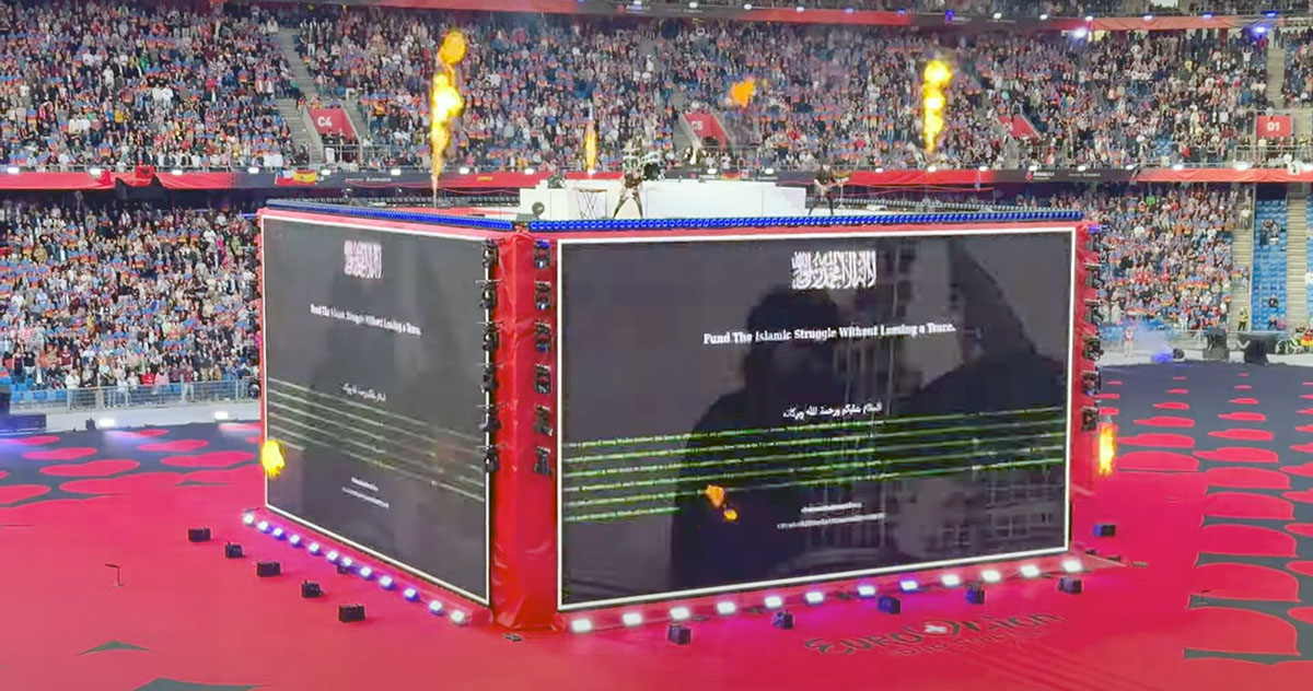 A screenshot of Baby Lasagna band performing "Rim Tim Tagi Dim" in Arena Plus, during a Eurovision pre-show at St. Jakob-Park stadium, atop a cube stage that displayed the message "Fund the Islamic Struggle Without Leaving a Trace"; screenshot from Point Switzerland YouTube footage by Pipeaway.