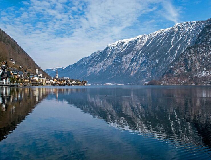 Reflective surface of Hallstätter See, lake by the picturesque Hallstatt town, with snow-peaked mountain in the background; photo by Ljubomir Žarković / Unsplash.
