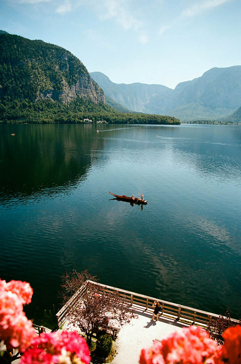 Small boat on a peaceful surface of Hallstätter See or Lake Hallstatt in Austria, as seen from a flowers-adorned lakeside terrace; photo by Benjamin Kaufmann / Unsplash.