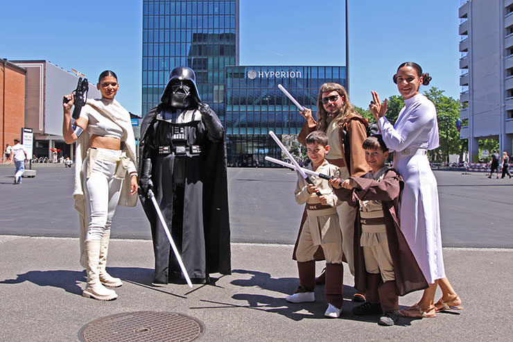 A family dressed up as "Star Wars" characters stands on Messeplatz, with Hyperion Hotel just behind, one of the closest accommodation options for attendees of Fantasy Basel, the Swiss Comic Con; photo by Ivan Kralj.