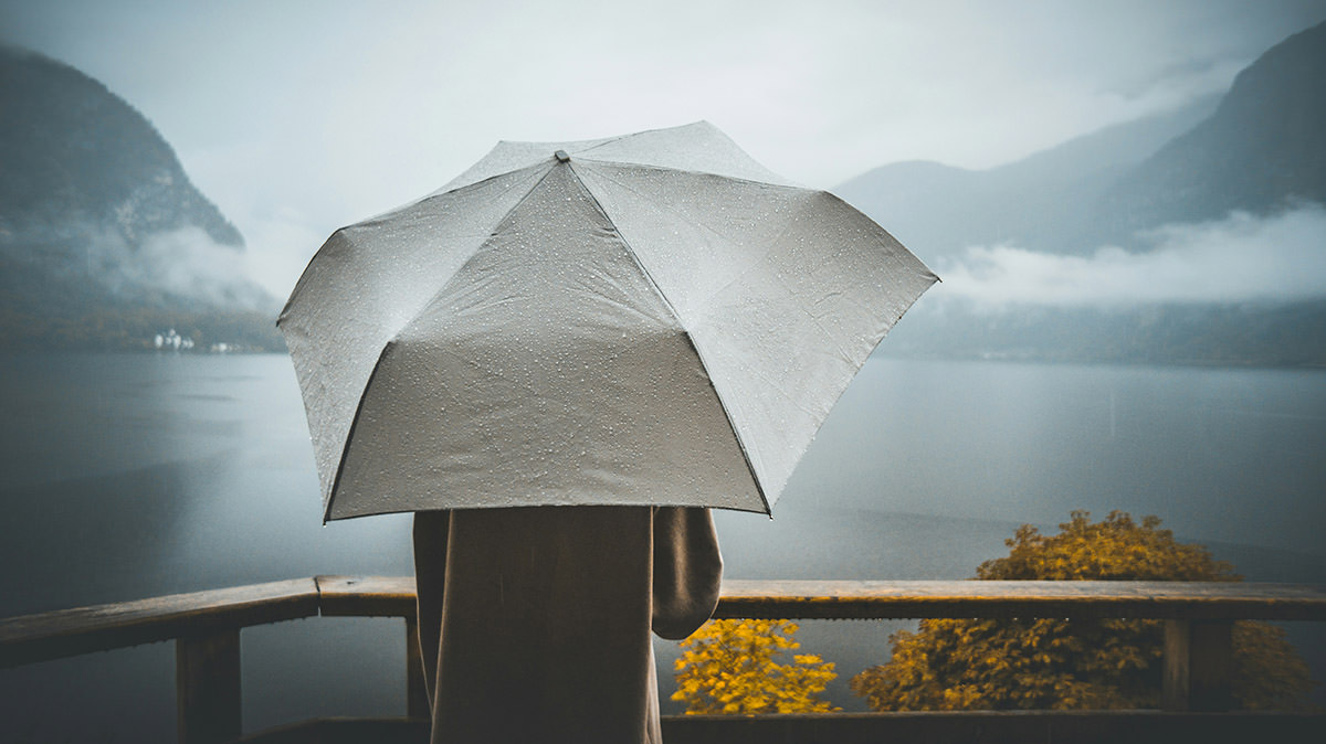 A person with an umbrella looking at a misty Hallstätter See lake in autumn, Austria; photo by Çağlar Canbay, Unsplash.