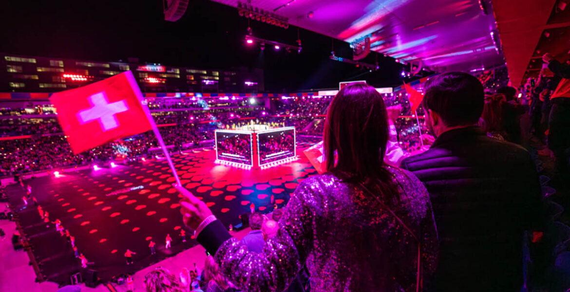 A visitor waving a Swiss flag at St. Jakob-Park stadium, the venue of Arena Plus pre-Eurovision party in Basel, Switzerland; photo by Mood Studios AG, Kanton Basel Stadt.
