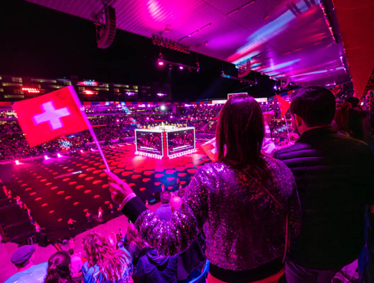 A visitor waving a Swiss flag at St. Jakob-Park stadium, the venue of Arena Plus pre-Eurovision party in Basel, Switzerland; photo by Mood Studios AG, Kanton Basel Stadt.