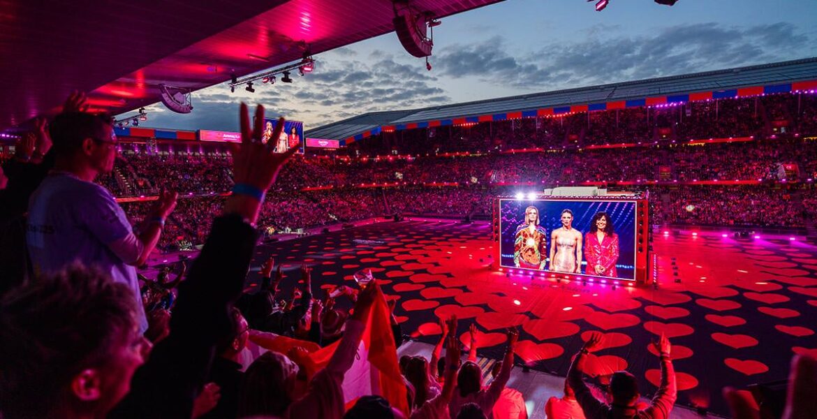 Eurovision hosts appearing on a gigantic cube screen at St. Jakob-Park, with delighted Arena Plus audiences; photo by Mood Studios AG, Kanton Basel-Stadt.
