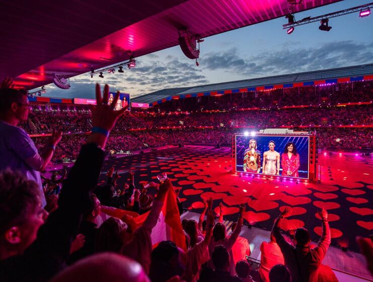 Eurovision hosts appearing on a gigantic cube screen at St. Jakob-Park, with delighted Arena Plus audiences; photo by Mood Studios AG, Kanton Basel-Stadt.