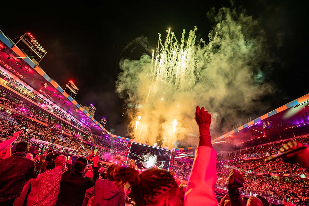An audience member raises a fist in the air as fireworks go on display at St. Jakob-Park stadium, during the Arena Plus Eurovision show; photo by Mood Studios AG, Kanton Basel-Stadt.