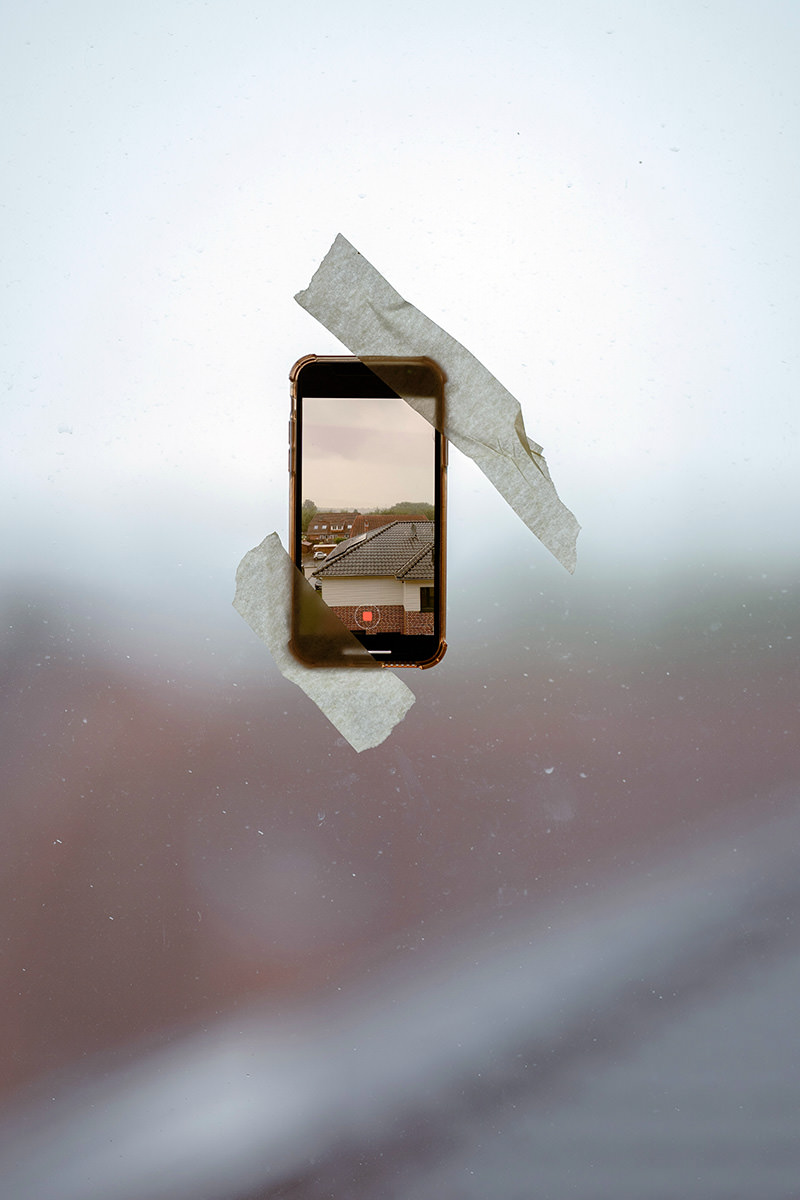 A smartphone shooting a cloudy weather outside while being attached for the window by two pieces of adhesive tape; photo by Omar Ramadan, Unsplash.