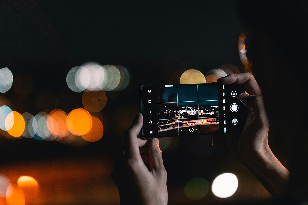 A person taking a picture of a city at night with a phone, with a "rule of thirds" grid; photo by Jiawei Zhao, Unsplash.