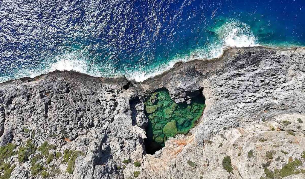 Bird's-eye view of the heart-shaped Green Lake or Prasini Limni on the rugged rocky coastline of Kythira Island in Greece; drone photo by Ivan Kralj.