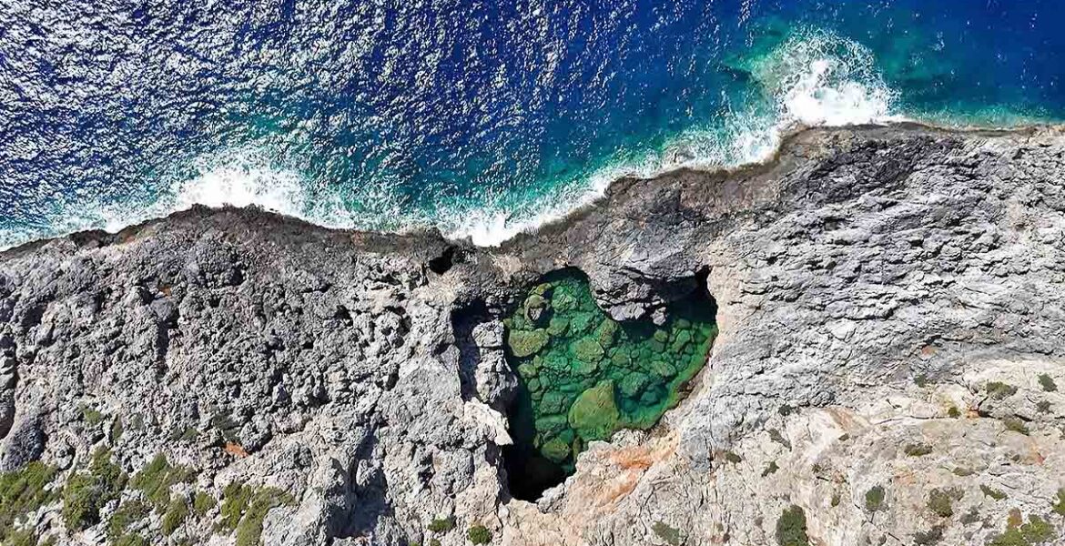 Bird's-eye view of the heart-shaped Green Lake or Prasini Limni on the rugged rocky coastline of Kythira Island in Greece; drone photo by Ivan Kralj.