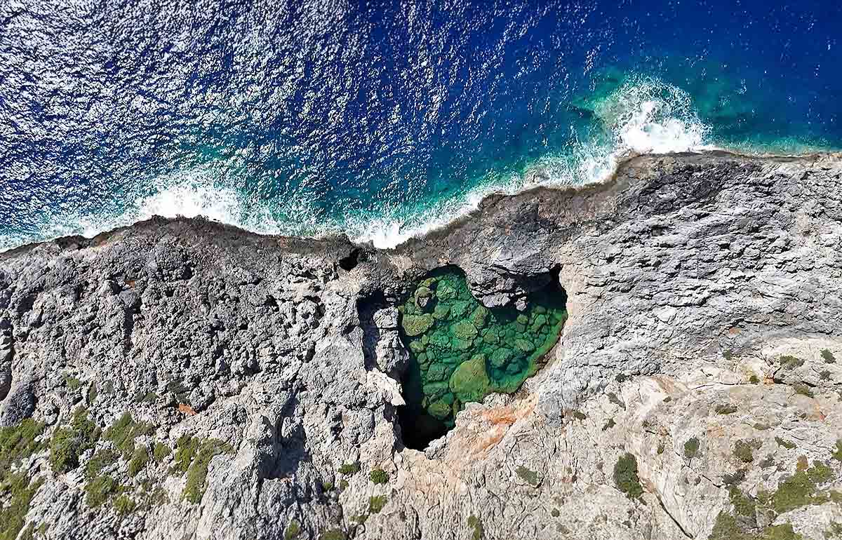 Bird's-eye view of the heart-shaped Green Lake or Prasini Limni on the rugged rocky coastline of Kythira Island in Greece; drone photo by Ivan Kralj.