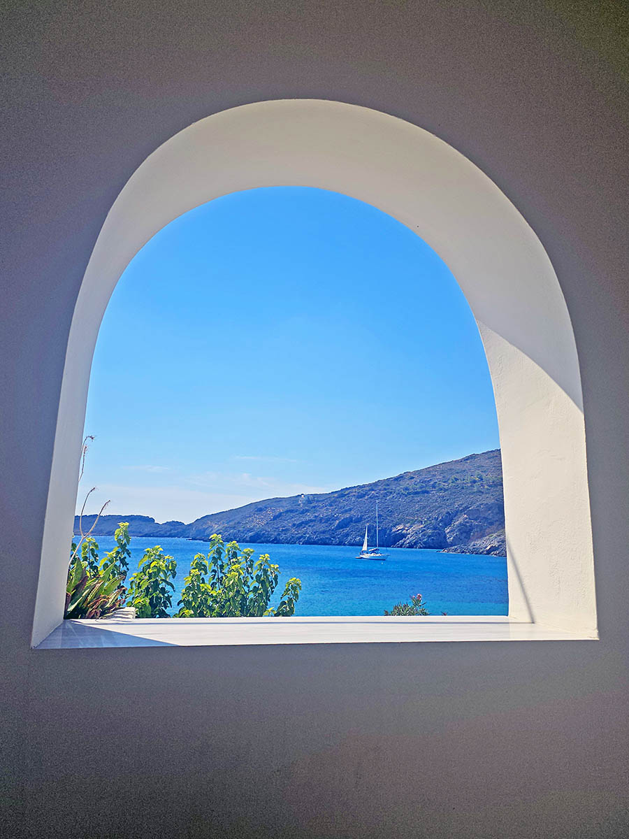 A view of Kapsali Bay with a boat, through a window of a beachfront house; photo by Ivan Kralj.