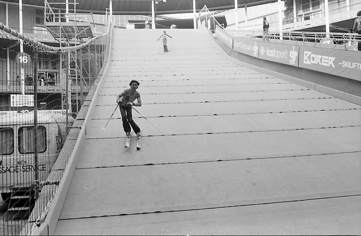 People on an artificial ski slope set in the Messe courtyard in Basel for Basler Herbstmesse, Basel Autumn Fair in 1975; photo by Willy Pragher, Staatsarchiv Freiburg.