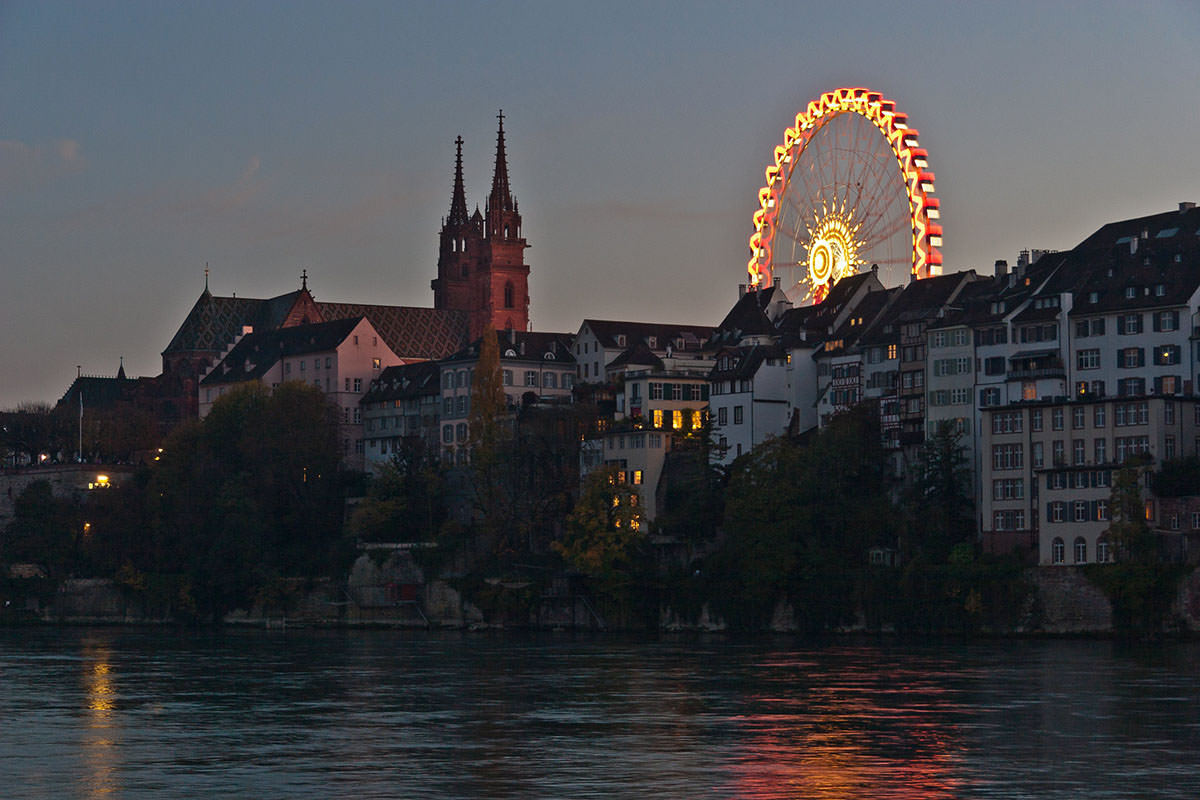 Riverside view of Basel Minster cathedral and the glowing Bellevue Ferris wheel set for Basler Herbstmesse, Basel Autumn Fair; photo by vivalatinoamerica.