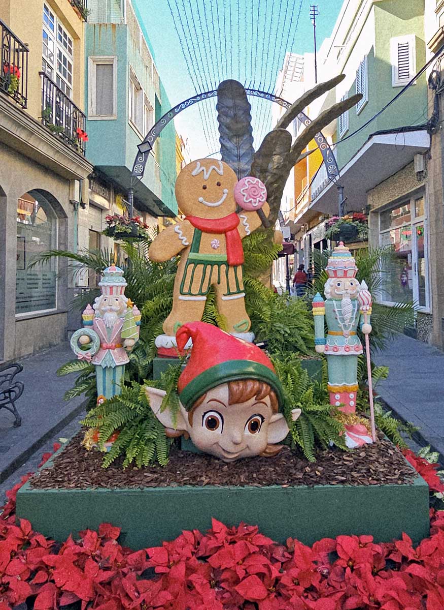Christmas decorations in the form of floral allegories in Calle Capitan Quesada, the main street in Gáldar, Ciudad Navidad - the scene includes a giant cookie, sweet nutcrackers and elf's head surrounded by festive plants; photo by Ivan Kralj.