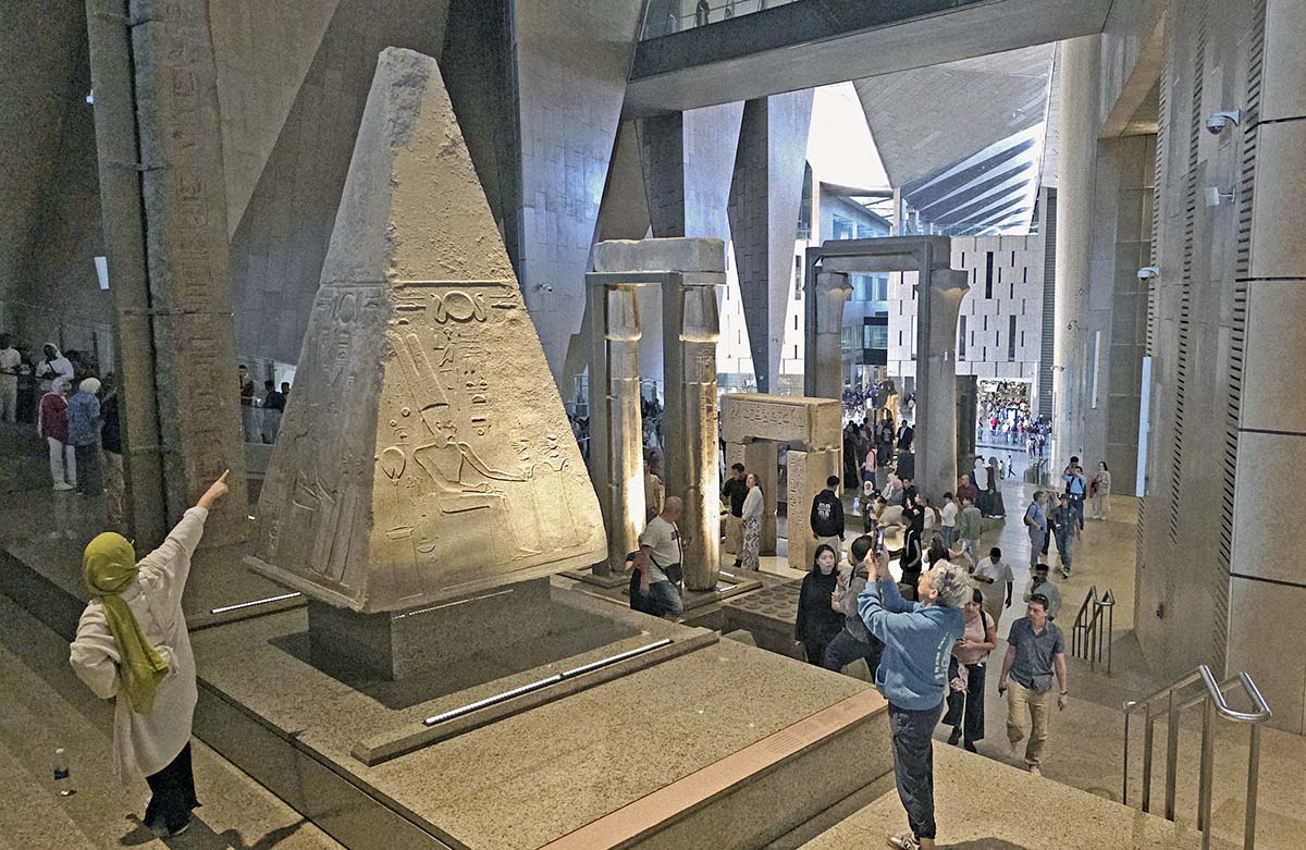 People pointing at and taking photographs of the pyramidion of an obelisk of Queen Hatshepsut, originally at the Temple of Amun-Re at Karnak, now on the Grand Stairs of the Grand Egyptian Museum in Giza, Egypt; photo by Ivan Kralj.