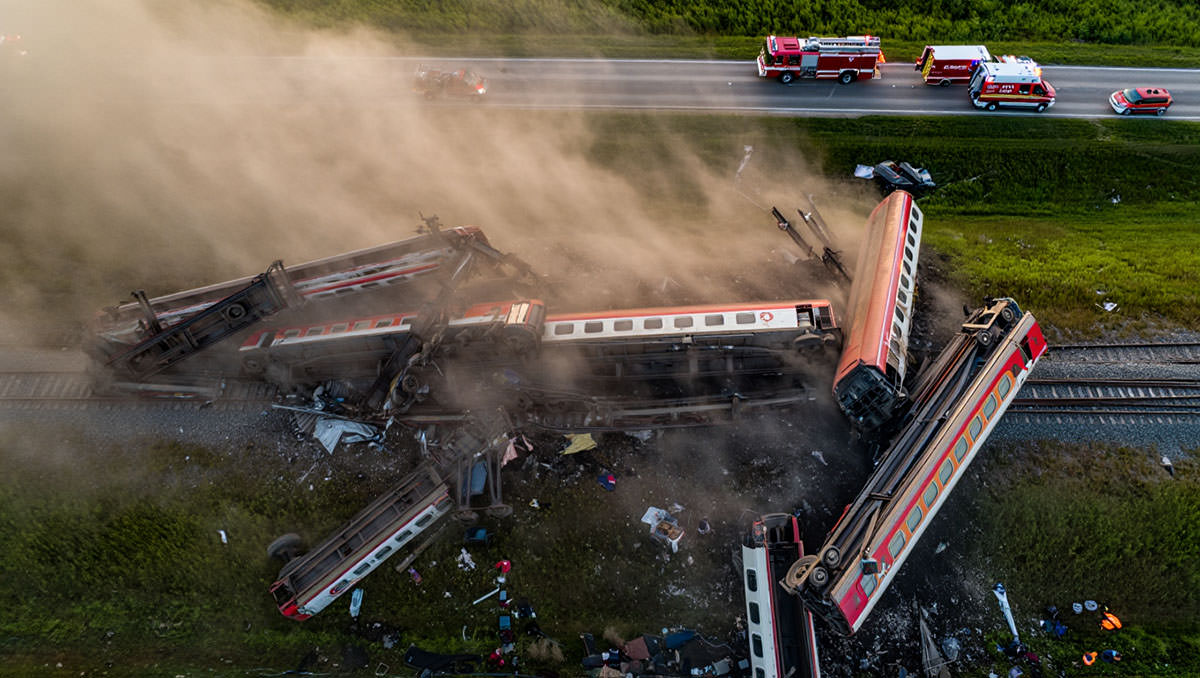 An aerial view of derailed train cars in a twisted wreckage, surrounded by emergency vehicles of first responders; AI image by Ivan Kralj / Reve.