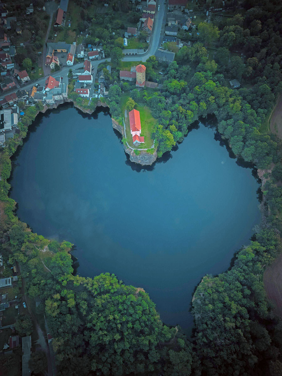 Aerial view of Kirchbruch See, a heart-shaped quarry lake in Brandis, Germany, with a medieval church, Bergkirche Beucha, perched on the cliff; photo by Martin Wischeropp, Pexels.